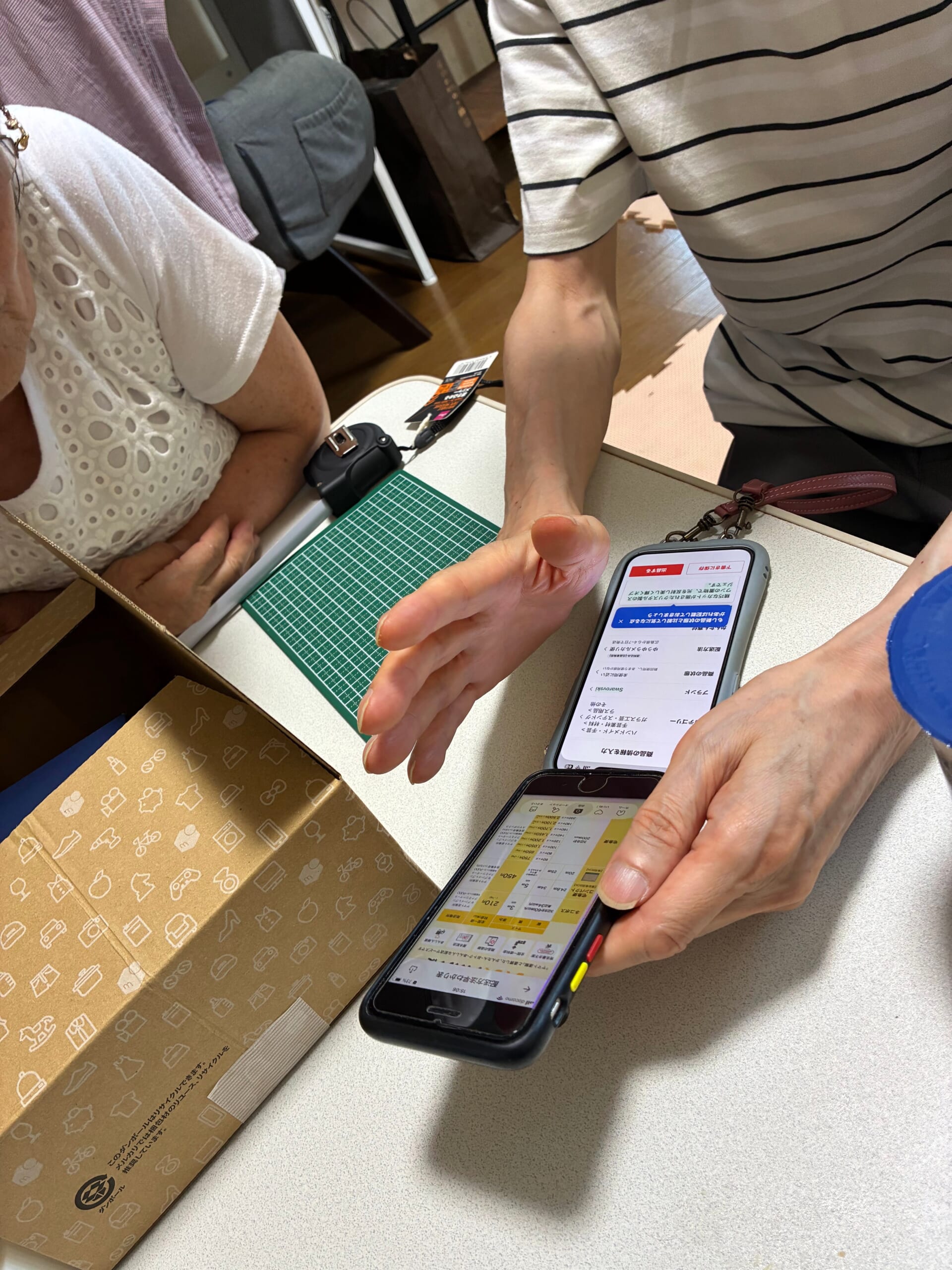 スマホ画面と実物の箱を見ながら梱包や発送方法を確認する授業の様子